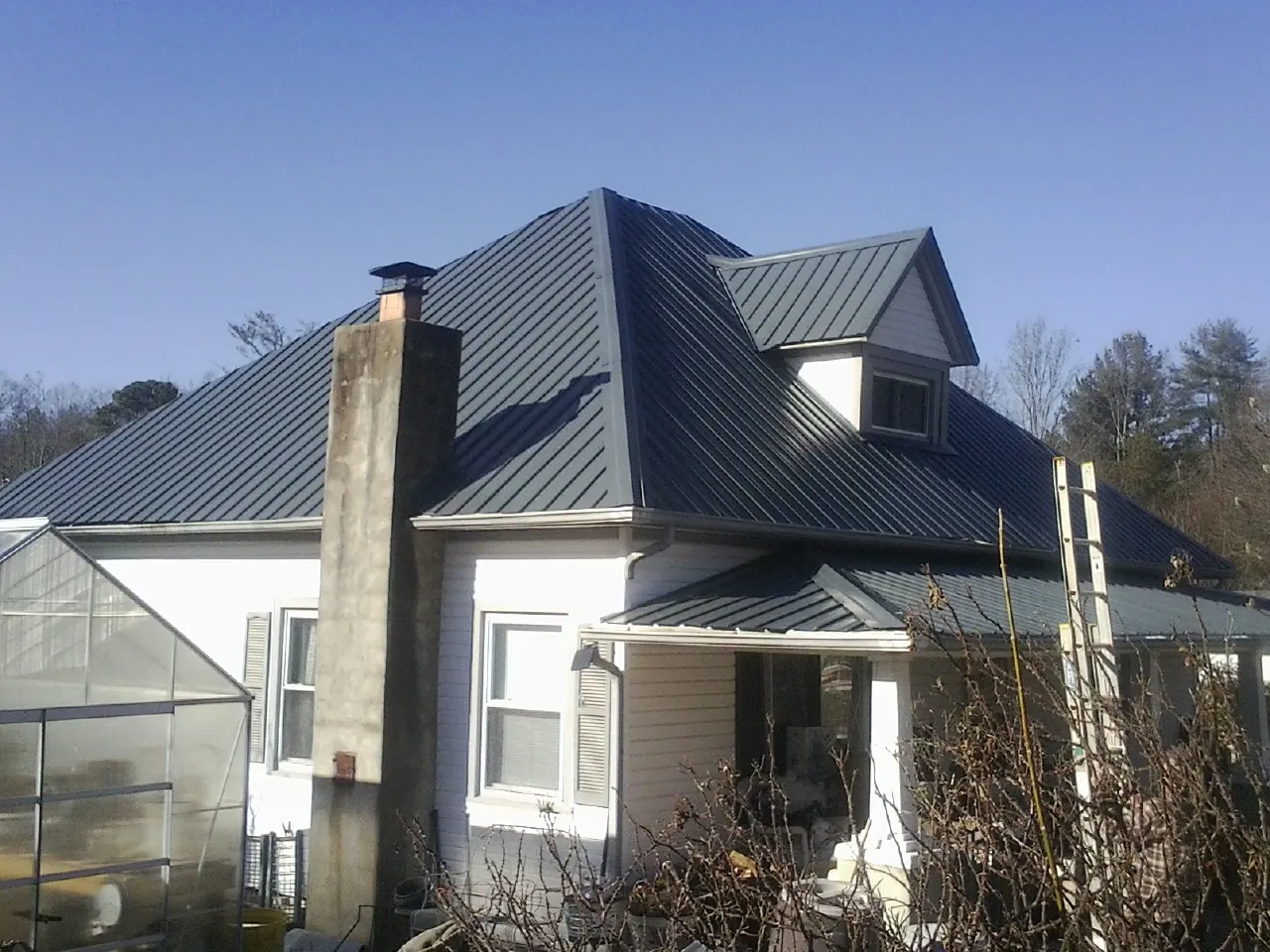 Dark blue standing seam metal roof on a white farmhouse with dormer — Slate & Tile Roof Repair by Roofing Brothers in Potwin