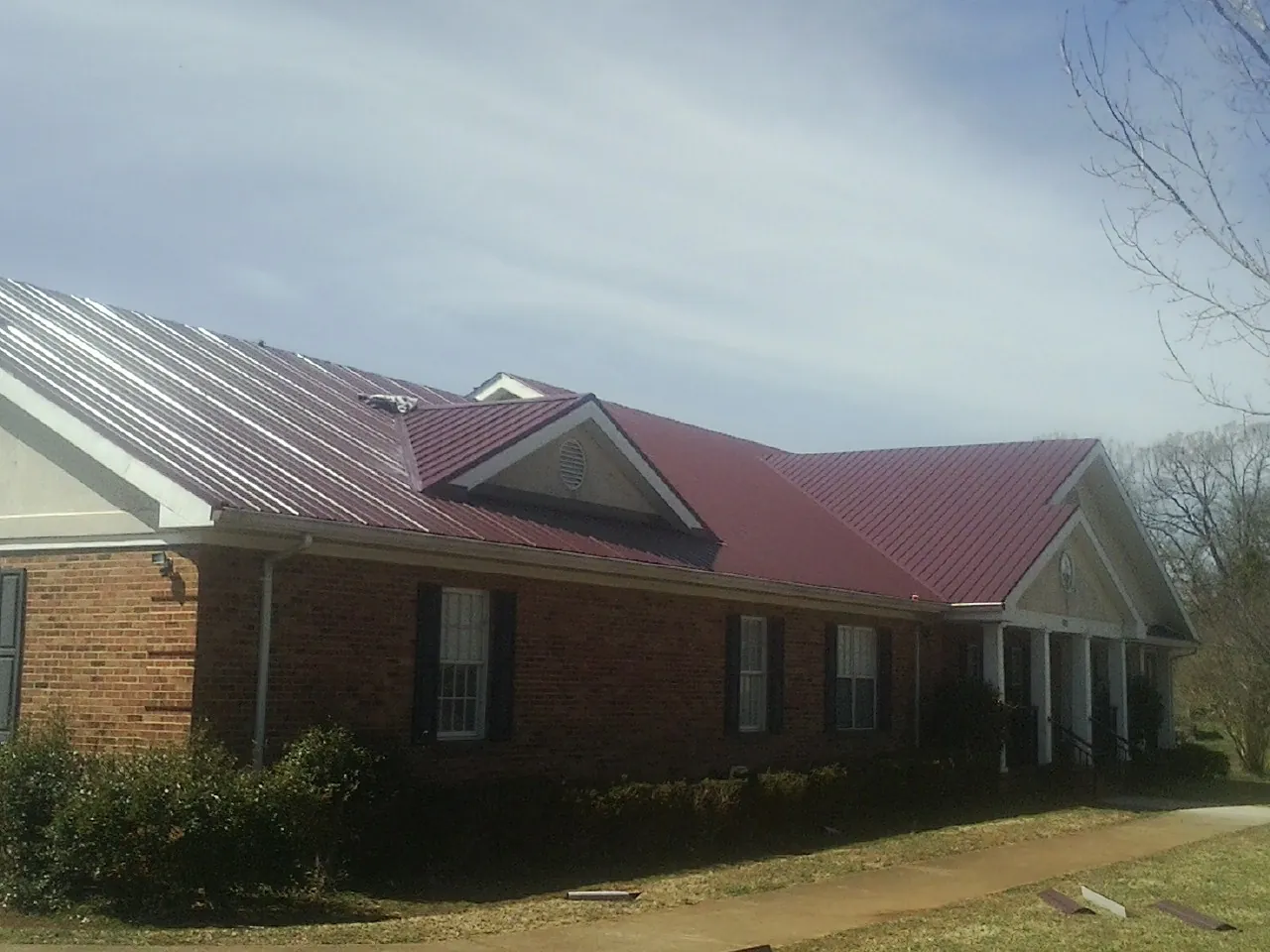 Red metal roof with gabled entries on a long brick building, from a Hail Damage Roof Repair job in Potwin