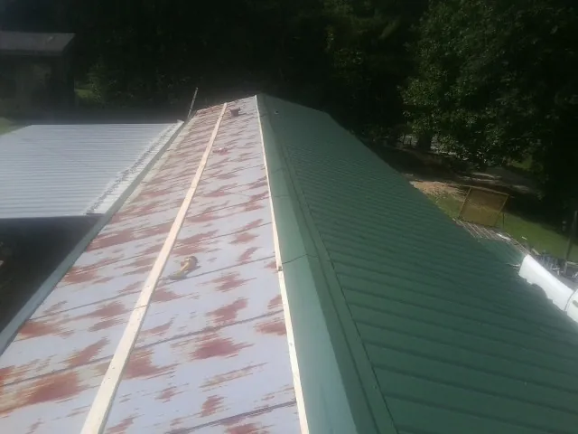 Old rusted panels beside newly installed green metal roofing — Wind Damage Roof Repair by Roofing Brothers in Potwin