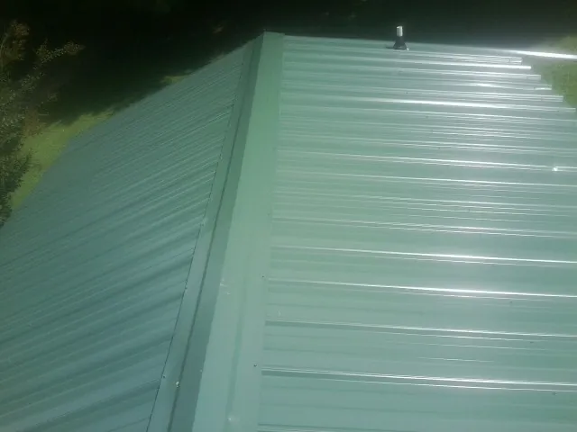 New green metal panels meeting at the ridge of a roof — Flat Roof Repair work by our crew in Potwin