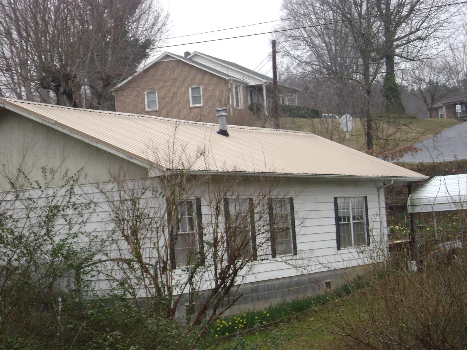 Tan metal roof on a white sided house set into a hillside — Commercial Roofing by Roofing Brothers in Potwin